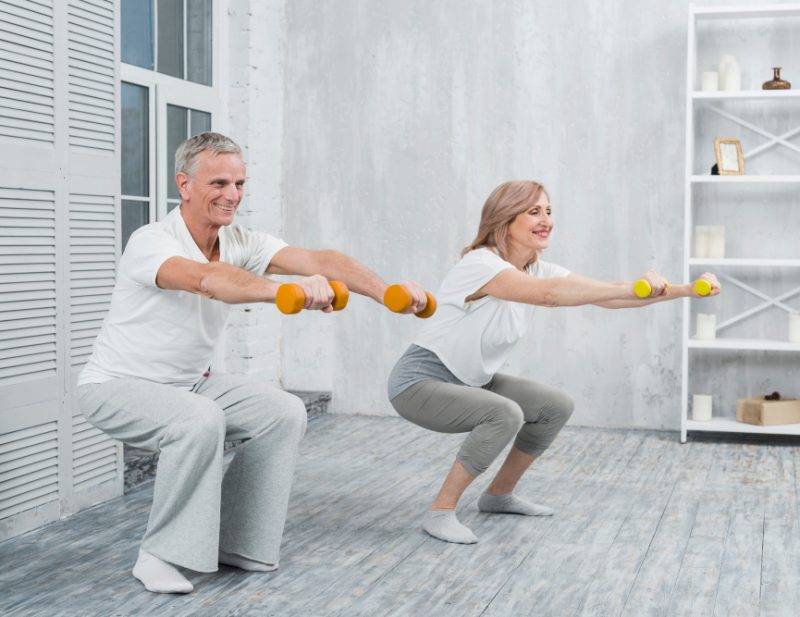 smiling-elder-couple-performing-exercise-with-dumbbells-home